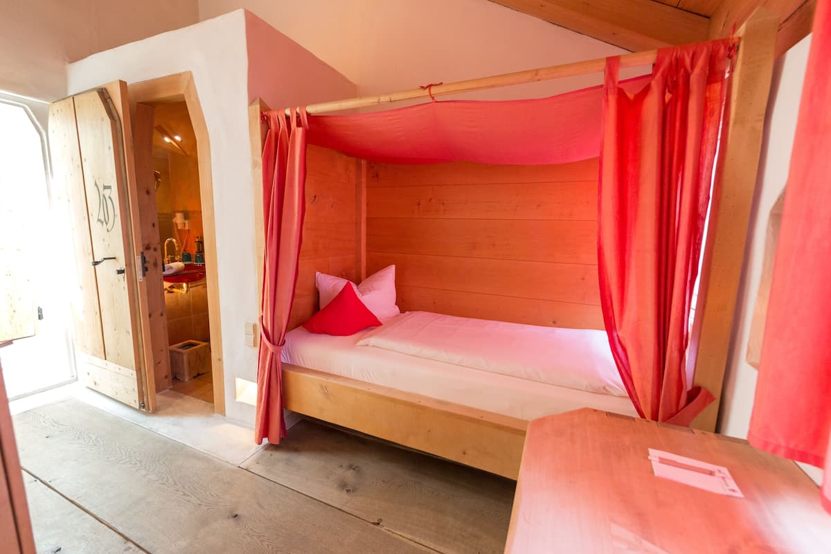 A wooden bunk bed with red curtains, a wooden door, and a small wooden stool in a room with wooden walls and floors.