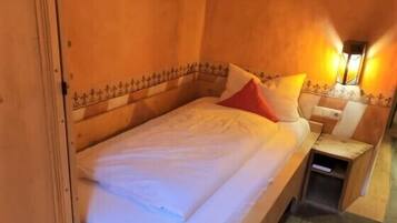 Een houten bed met wit beddengoed en een rode kussen in een kamer met houten wanden en een nachtkastje.