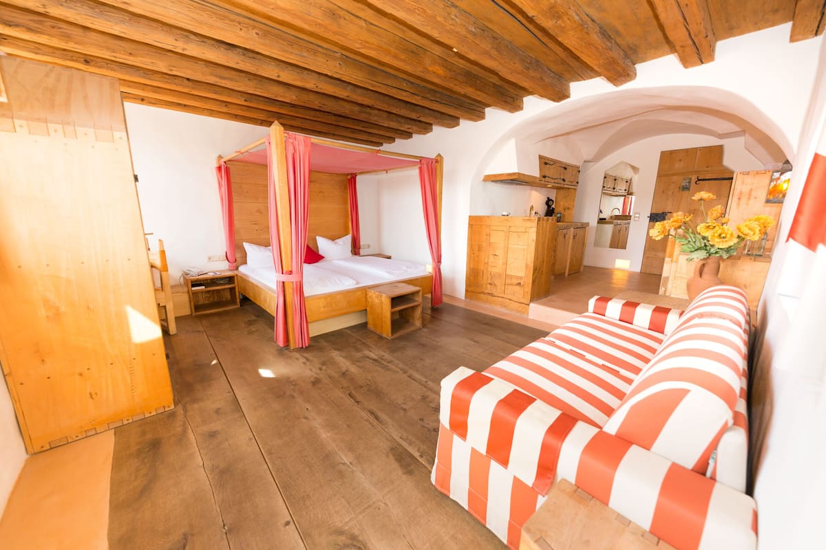 A bedroom with a four-poster bed, a wooden bench, and a striped sofa.