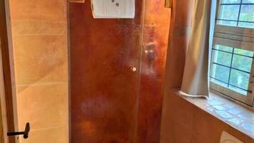 Een badkamer met douche, toilet en raam met gordijnen.