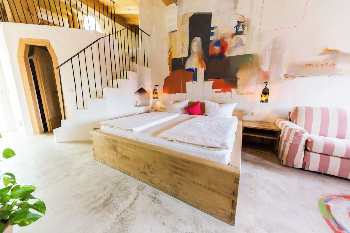 A bedroom with a wooden bed, a staircase, a painting on the wall, and a striped sofa.