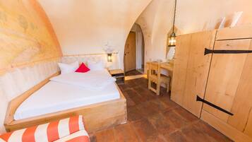 A cozy bedroom with a wooden bed, a desk, and a chair, featuring a rustic ceiling and wooden walls.