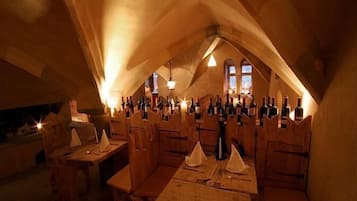 Une pièce mansardée avec des tables et des chaises en bois, des bouteilles de vin et un lustre.