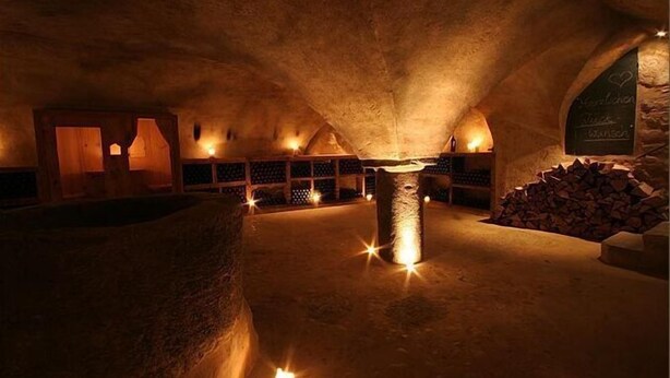 An underground room with stone walls, a central pillar, and shelves with items. - Hotel San Gabriele (Rosenheim)