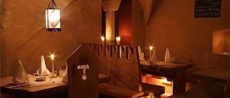 Un intérieur rustique à la lumière tamisée, avec des tables et des bancs en bois, des bougies et un menu écrit à la craie.