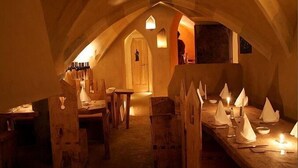 A dimly lit, vaulted room with wooden tables and chairs, a wooden bench, and a long table with candles and paper boats. - Hotel San Gabriele (Rosenheim)