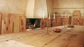 A wooden dining table with a central candle holder, a fireplace, and a rustic wooden wall.