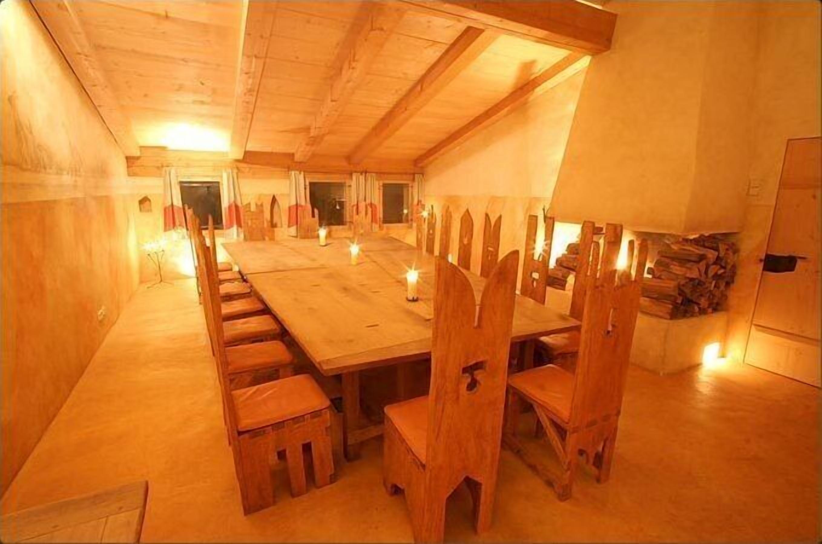 A long wooden dining table with chairs, candles, and a fireplace in a warmly lit room.