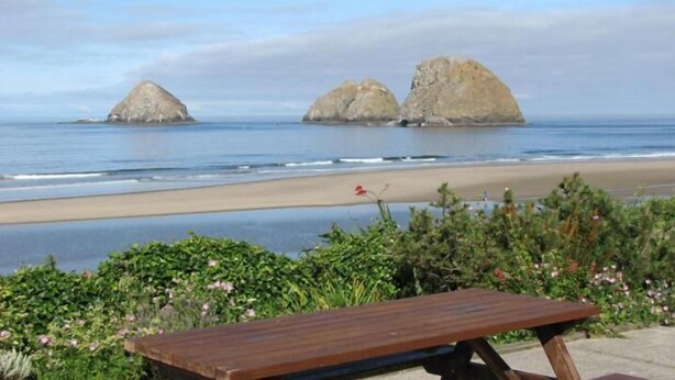 A wooden bench overlooking a beach with three large rock formations in the distance. - Summer Wind Budget Motel (Newport)