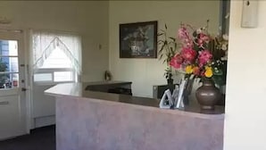 A reception area with a reception desk, a framed artwork on the wall, and a vase with flowers. - Summer Wind Budget Motel (Newport)