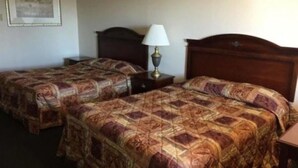 A hotel room with two single beds, each with a patterned bedspread. There is a nightstand with a lamp between the beds. - Summer Wind Budget Motel (Newport)