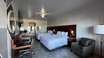 A hotel room with a large bed, a desk, a chair, a lamp, and a ceiling fan.
