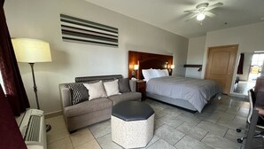 Habitación de hotel con cama, sofá, reposapiés pequeño, escritorio y ventilador de techo.