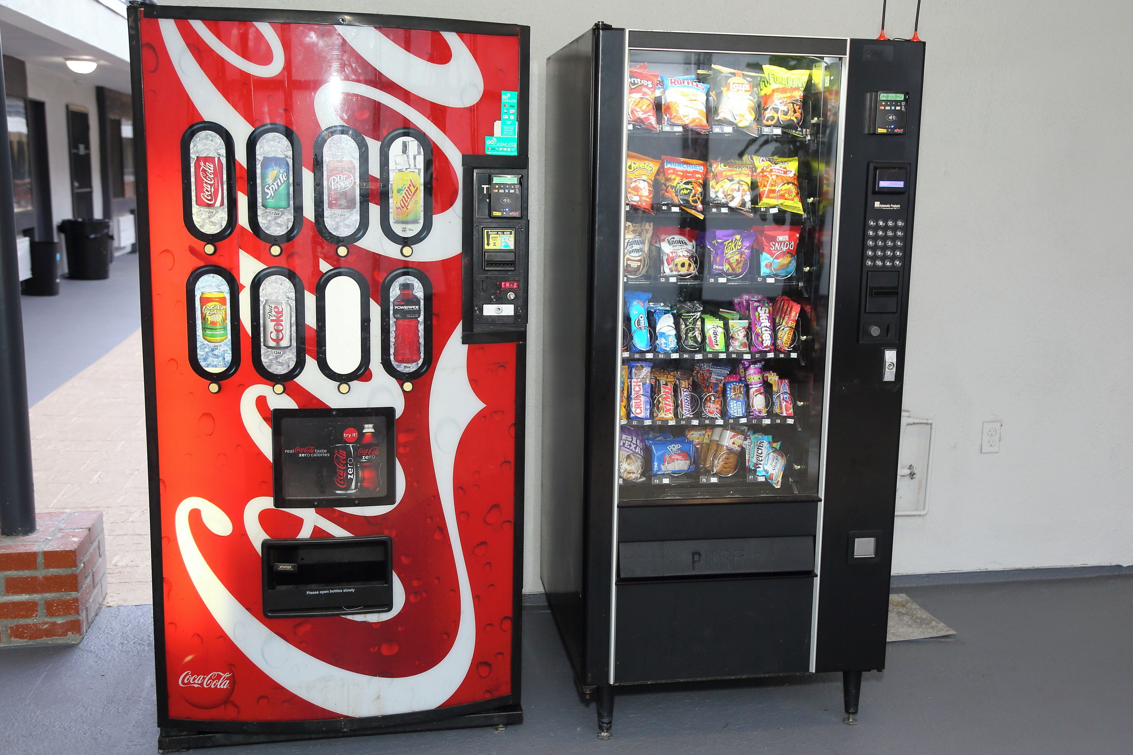 Two vending machines, one with a Coca-Cola logo and the other with a variety of snacks.