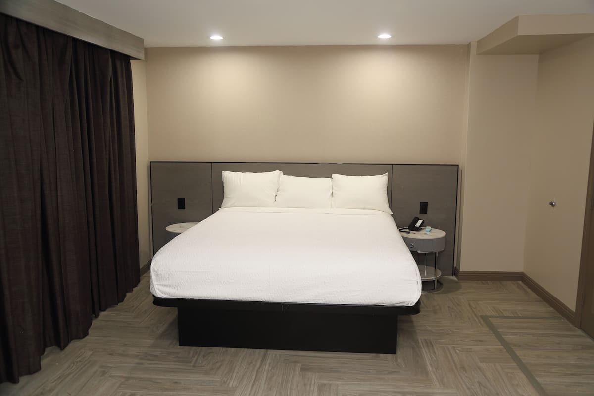 A hotel room with a large bed, two bedside tables, a headboard, and a curtain.