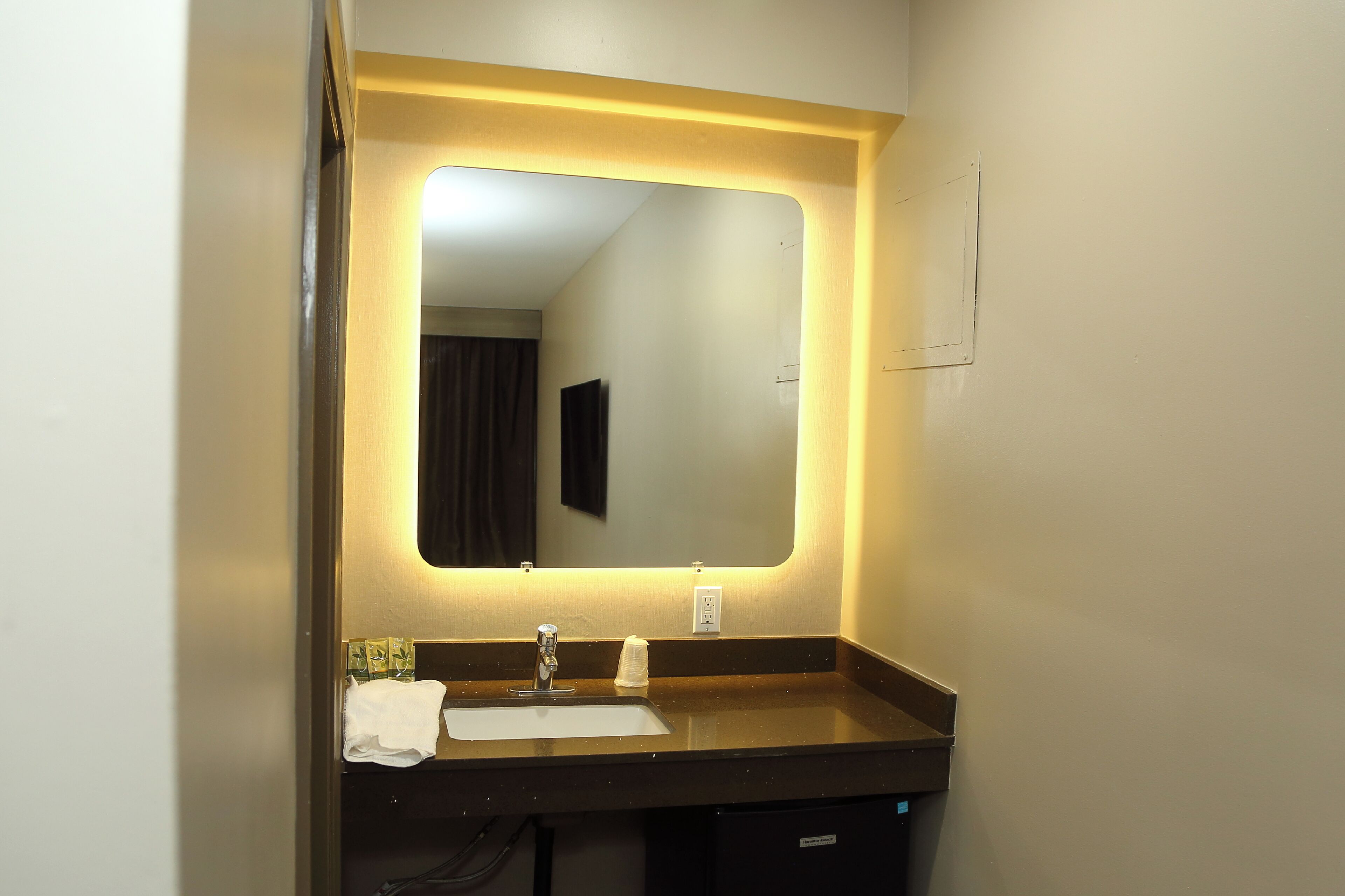 A hotel bathroom with a mirror, sink, and towel rack.