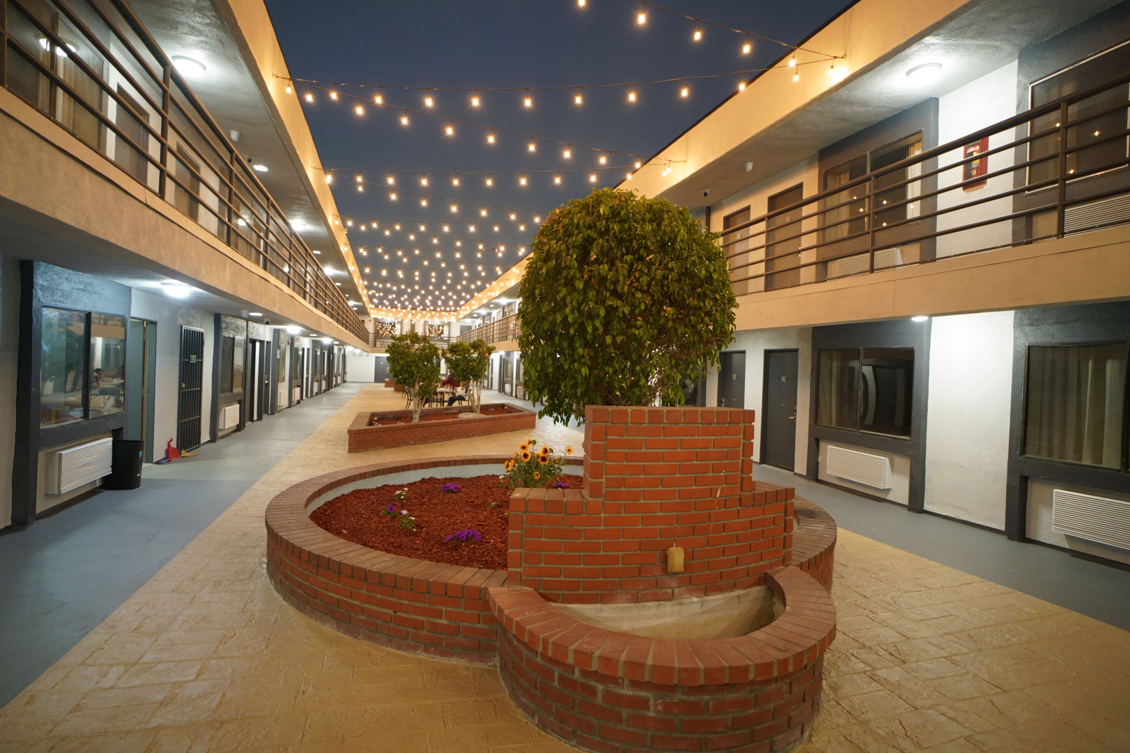 A spacious indoor area with a central brick planter, multiple windows, and a ceiling adorned with string lights.