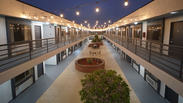 A multi-level hotel corridor with a central walkway, railings, and a seating area with tables and chairs. - Gardena Terrace Inn (Gardena)