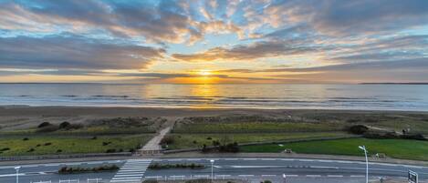 Een kustweg met een zebrapad, een grasveld en een ondergaande zon boven de zee.