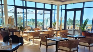 Ein Restaurant mit Korbmöbeln, großen Fenstern und Meerblick.