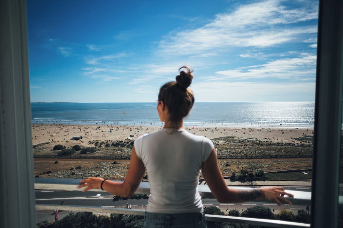 Eine Person blickt vom Balkon auf einen Strand.