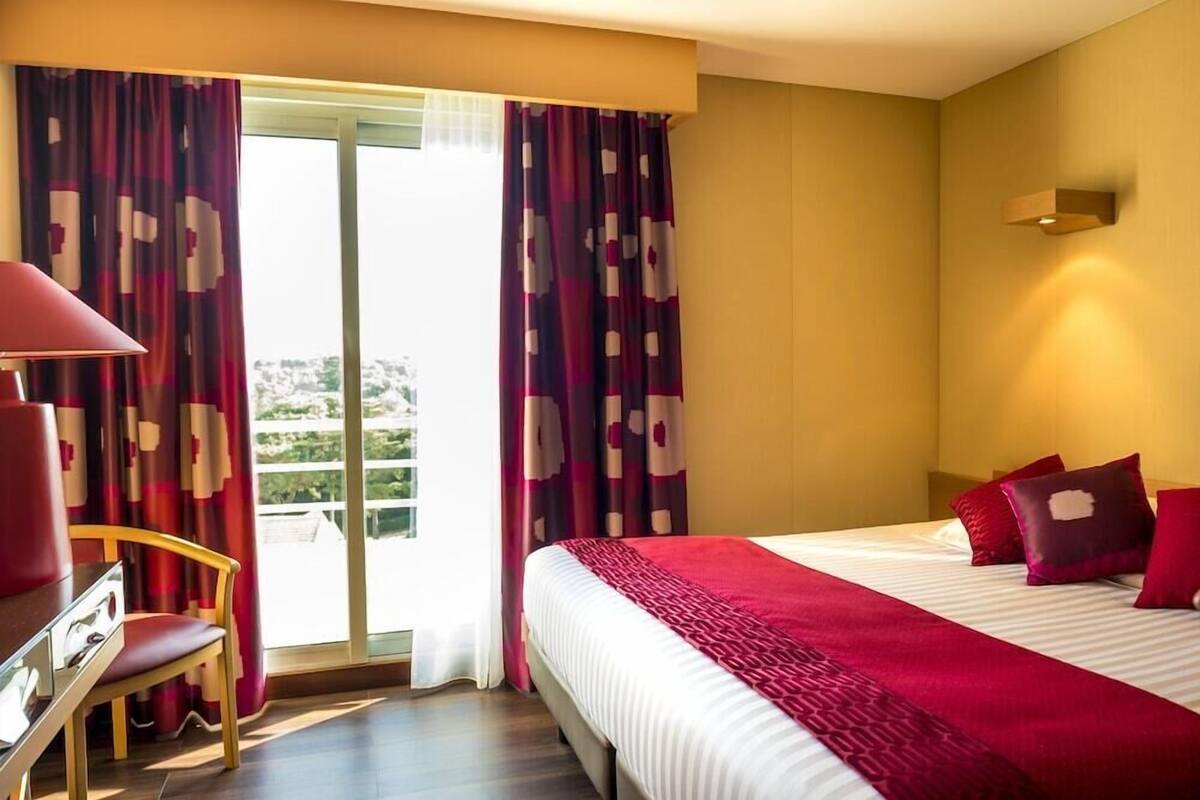 Ein Hotelzimmer mit Bett, Schreibtisch, Stuhl und Blick durch eine Glastür.