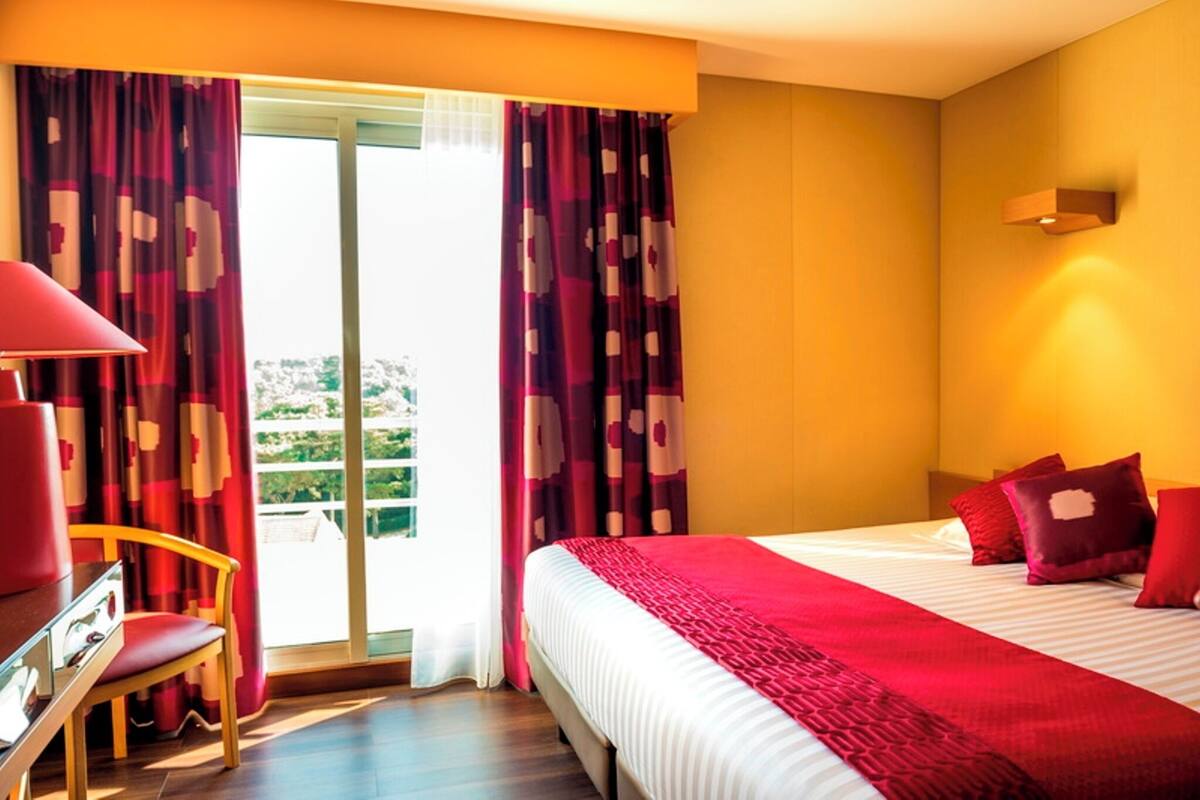 Ein Hotelzimmer mit Bett, Schreibtisch, Stuhl und Blick durch eine Glastür.