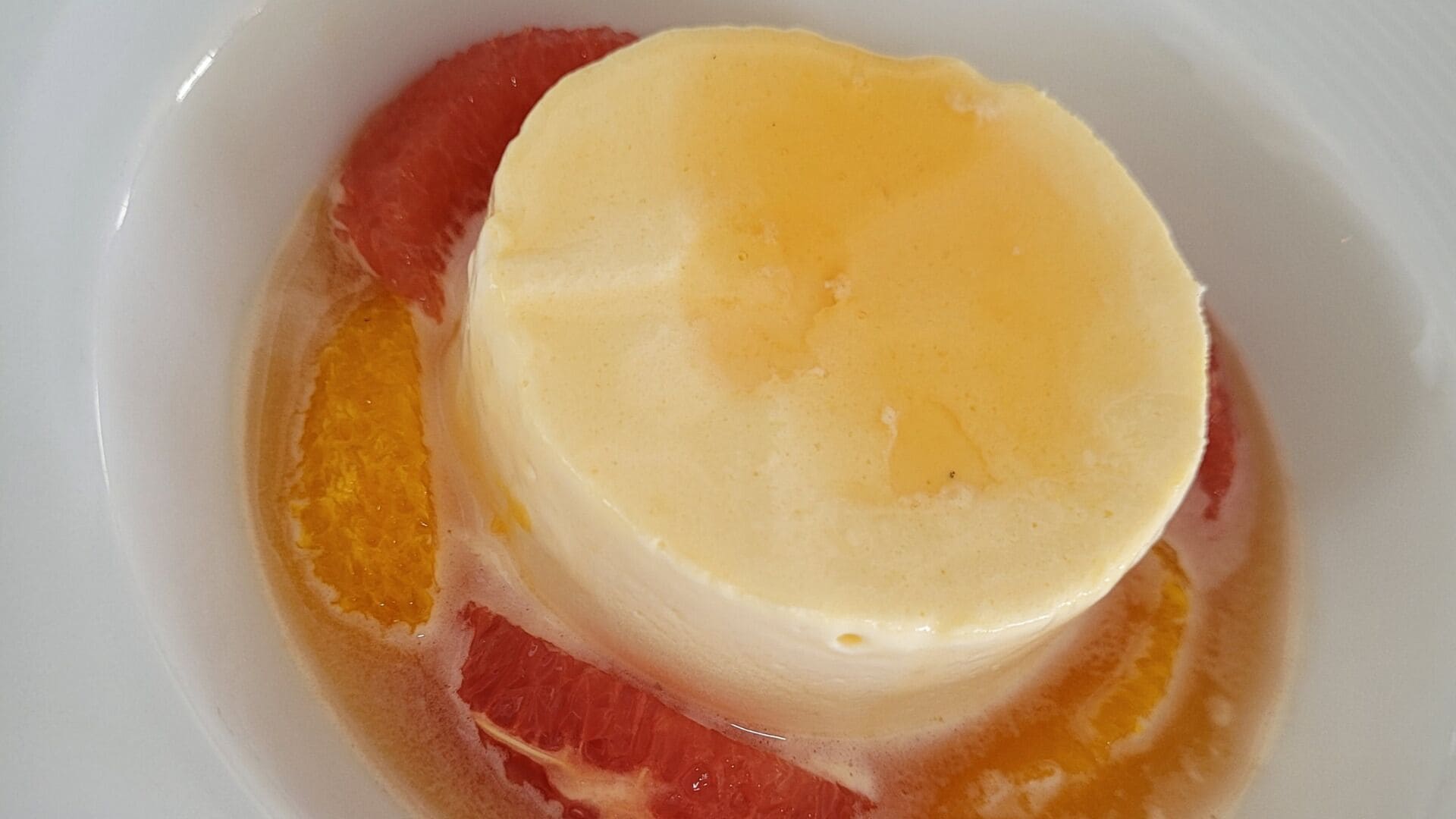 A white bowl containing a yellow dessert with a red fruit slice.