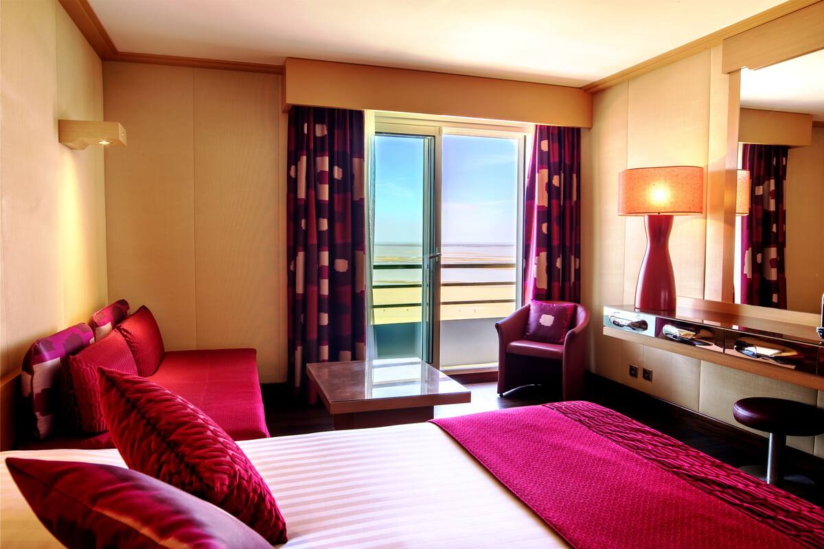 Ein Hotelzimmer mit Bett, Schreibtisch, Stuhl und Meerblick aus dem Fenster.