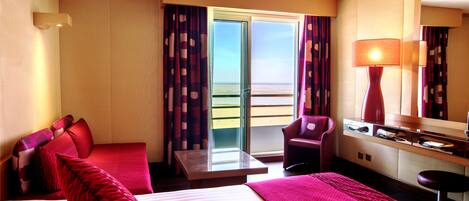A hotel room with a bed, a desk, a chair, and a view of the sea through the window.