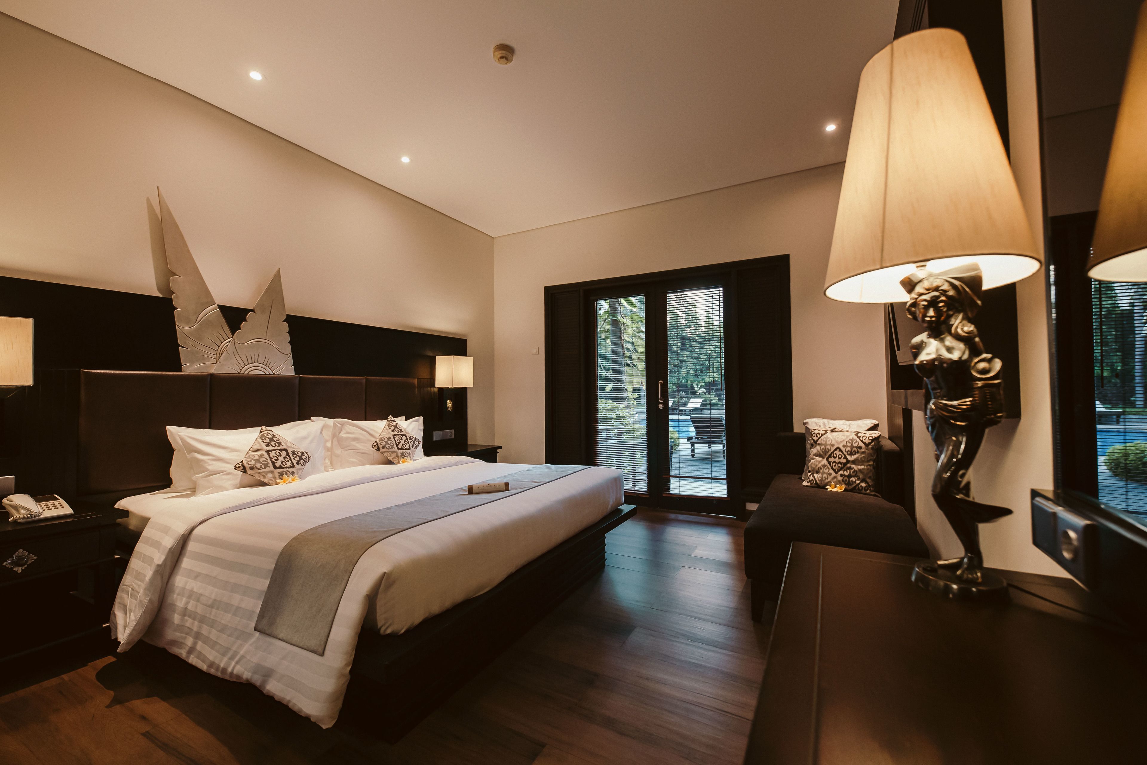 A modern hotel room with a large bed, a nightstand, a desk, and a statue.