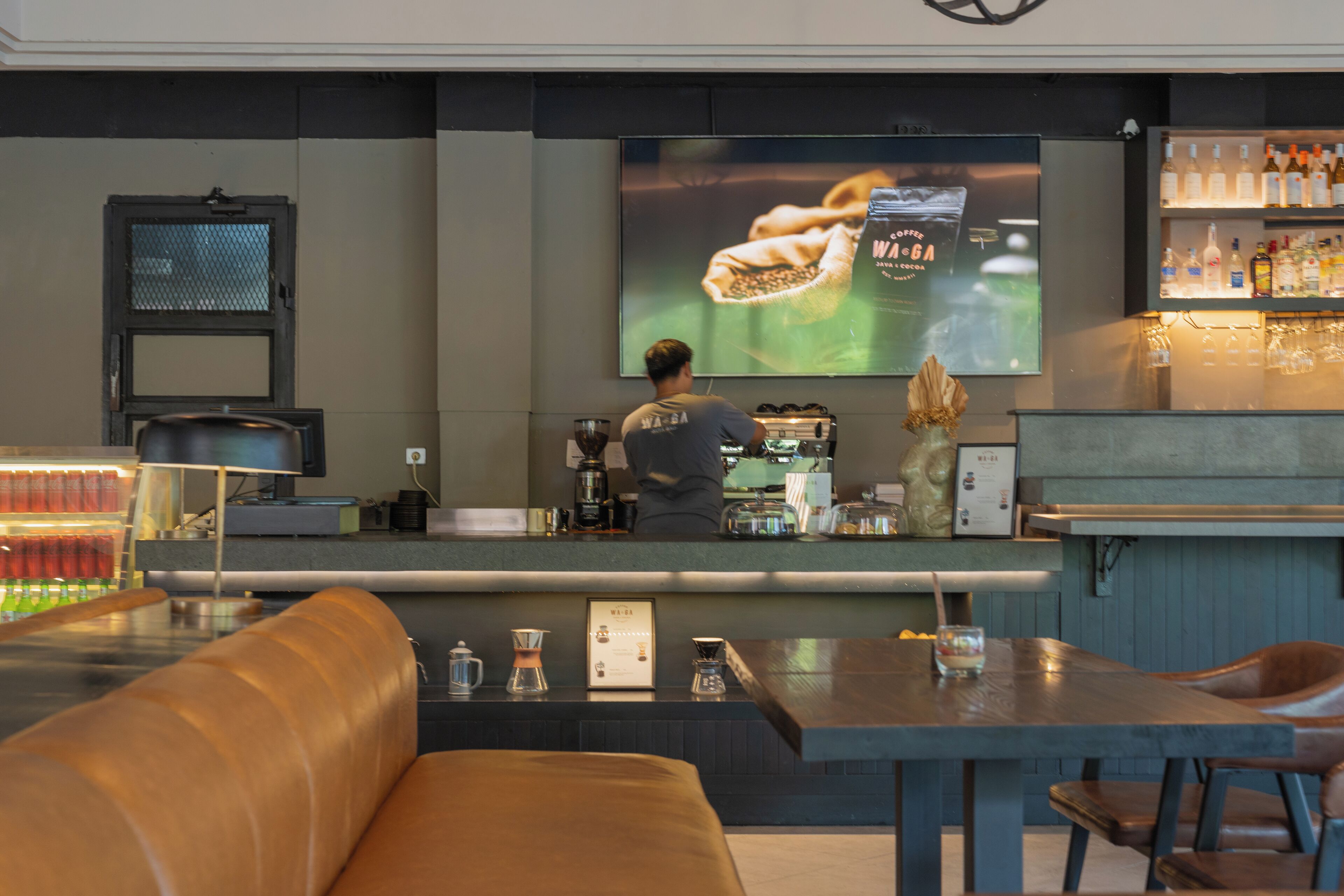 A bar area with a counter, seating, and a television screen displaying a coffee advertisement.