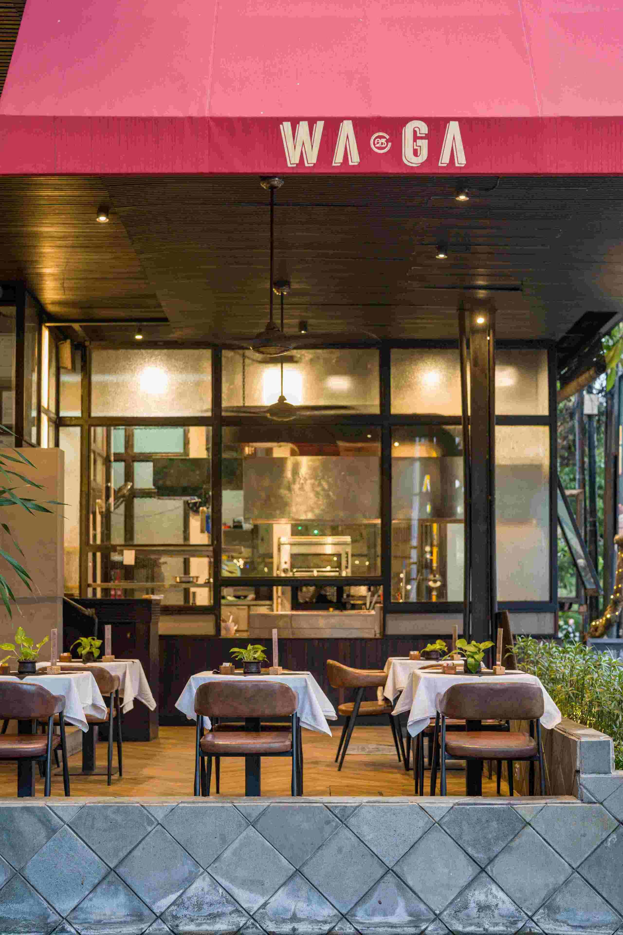 An outdoor dining area with tables and chairs, a kitchen visible through the glass, and a red awning with the text "WA GA".