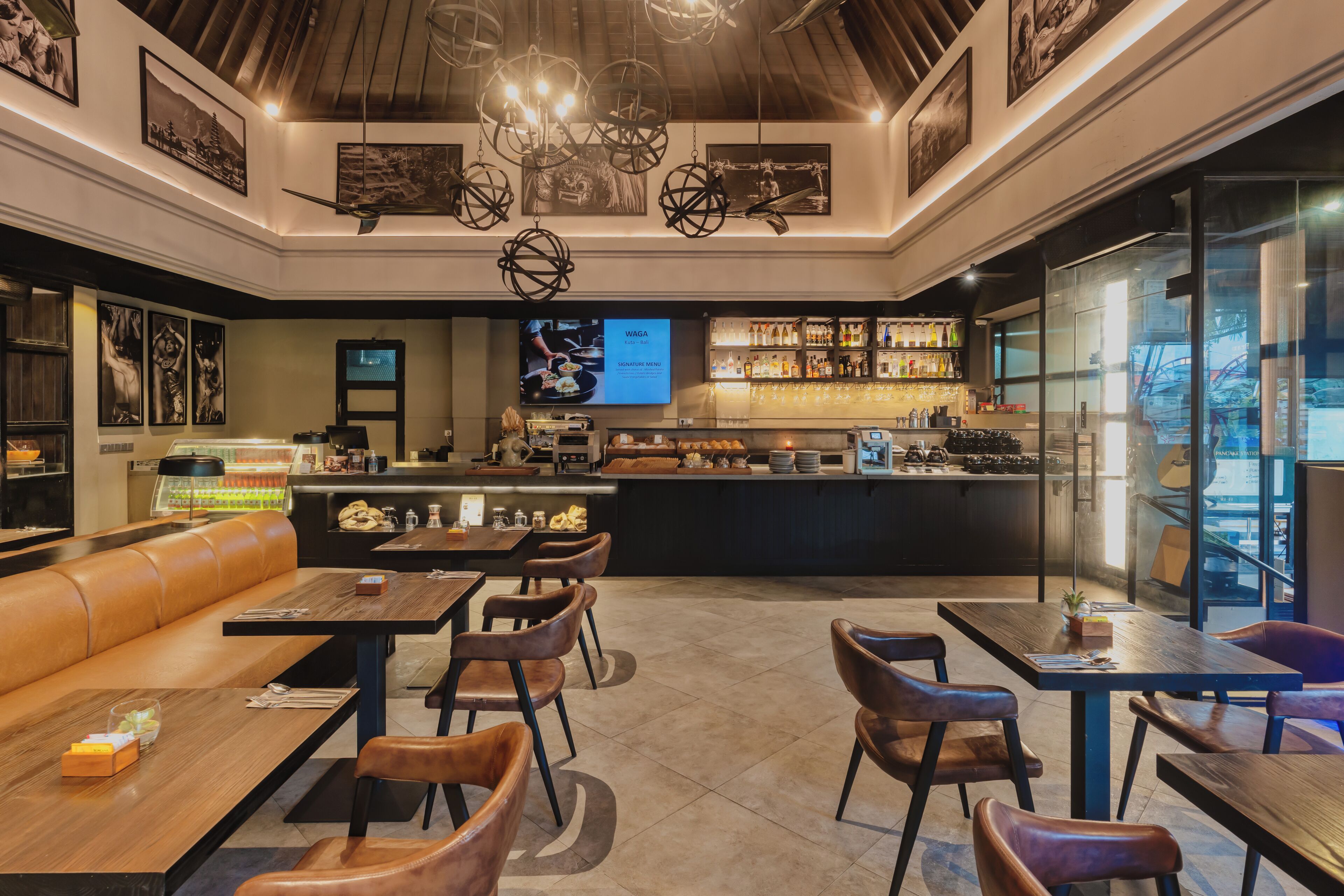 Um restaurante moderno com área de bar, mesas e cadeiras de madeira e uma tela grande exibindo conteúdo.