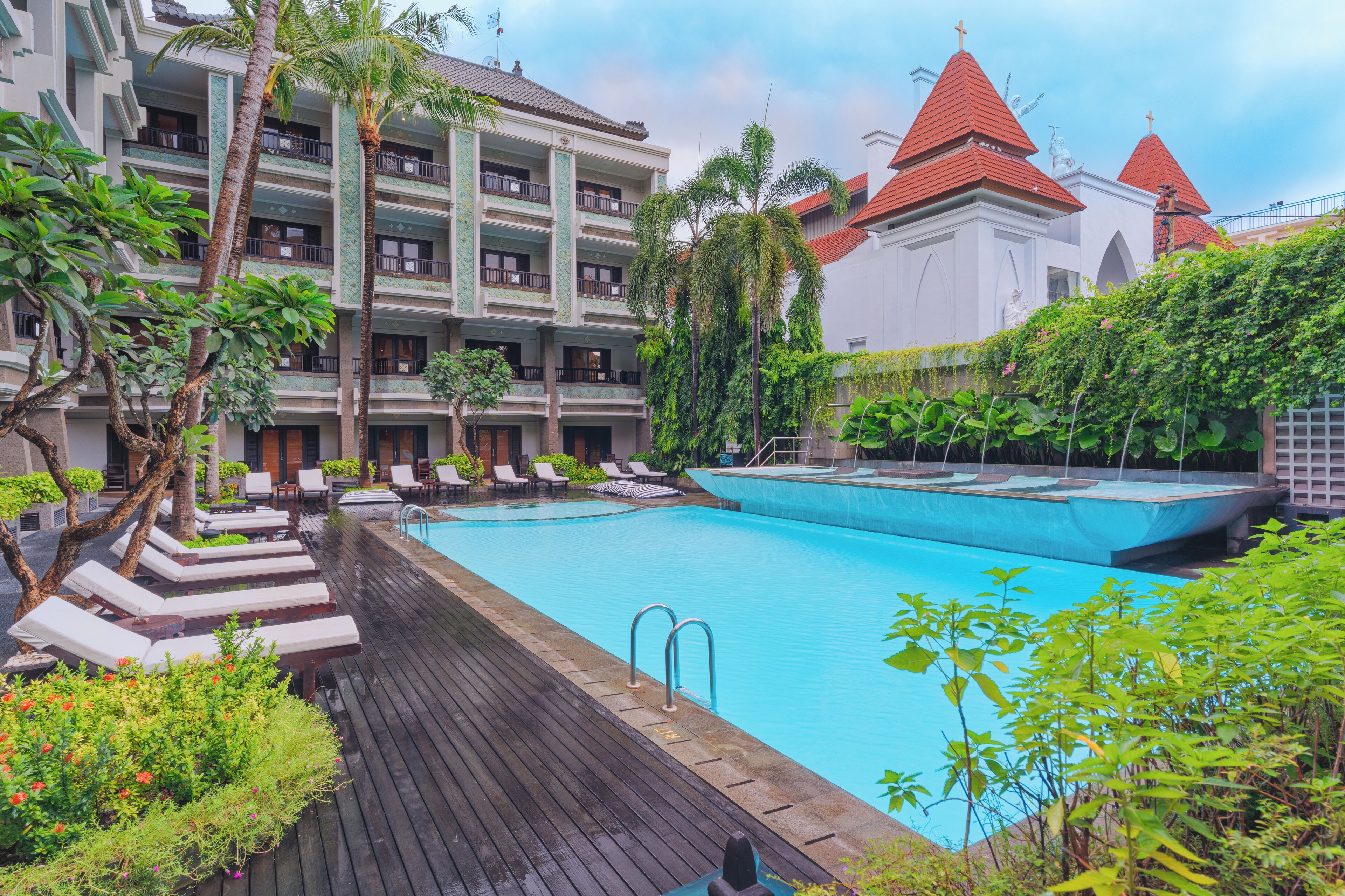 Un hotel con piscina, sillas de descanso y un jardín tropical.