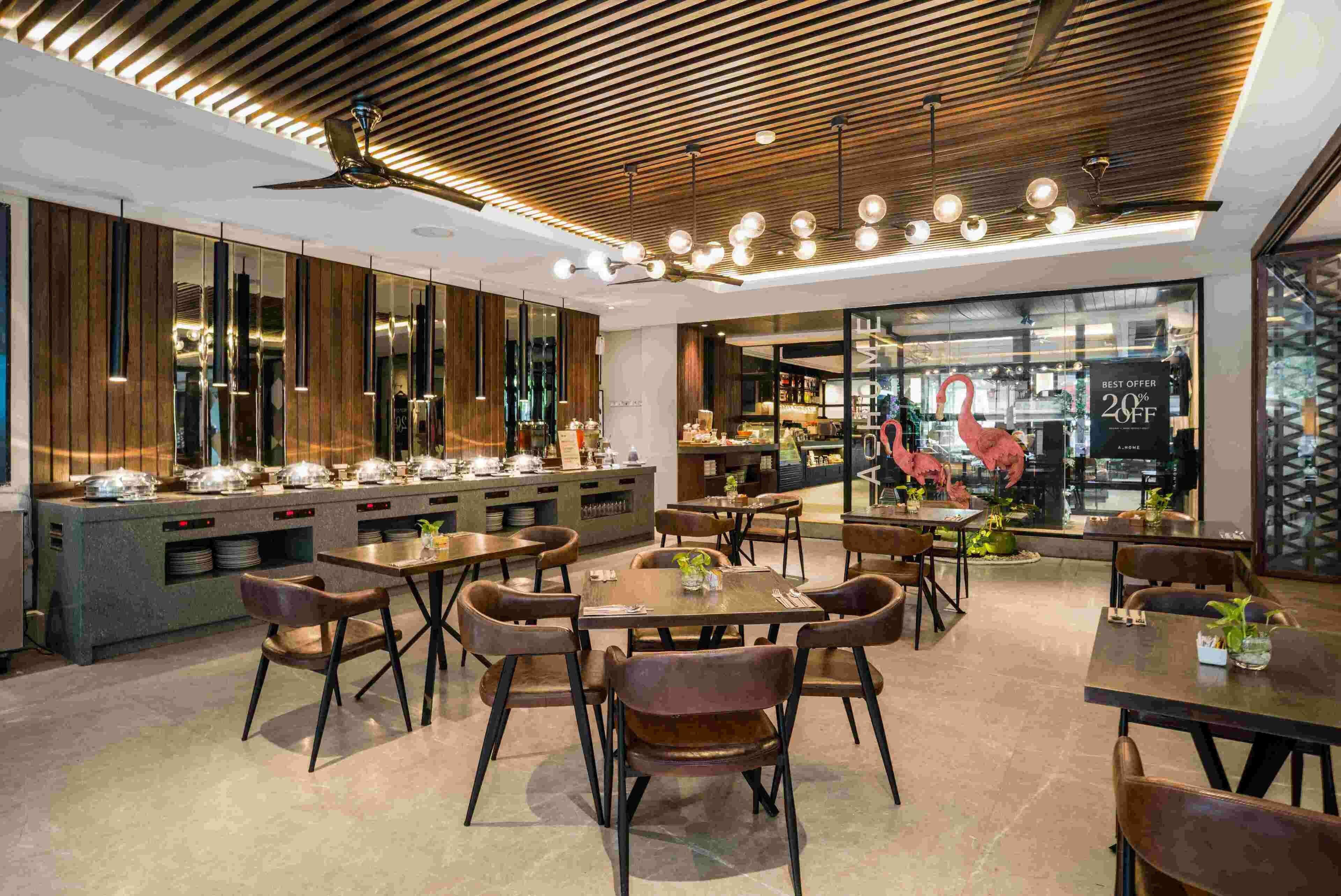 Un interior de restaurante moderno con paneles de techo de madera, iluminación colgante y una zona de comedor central con mesas y sillas.