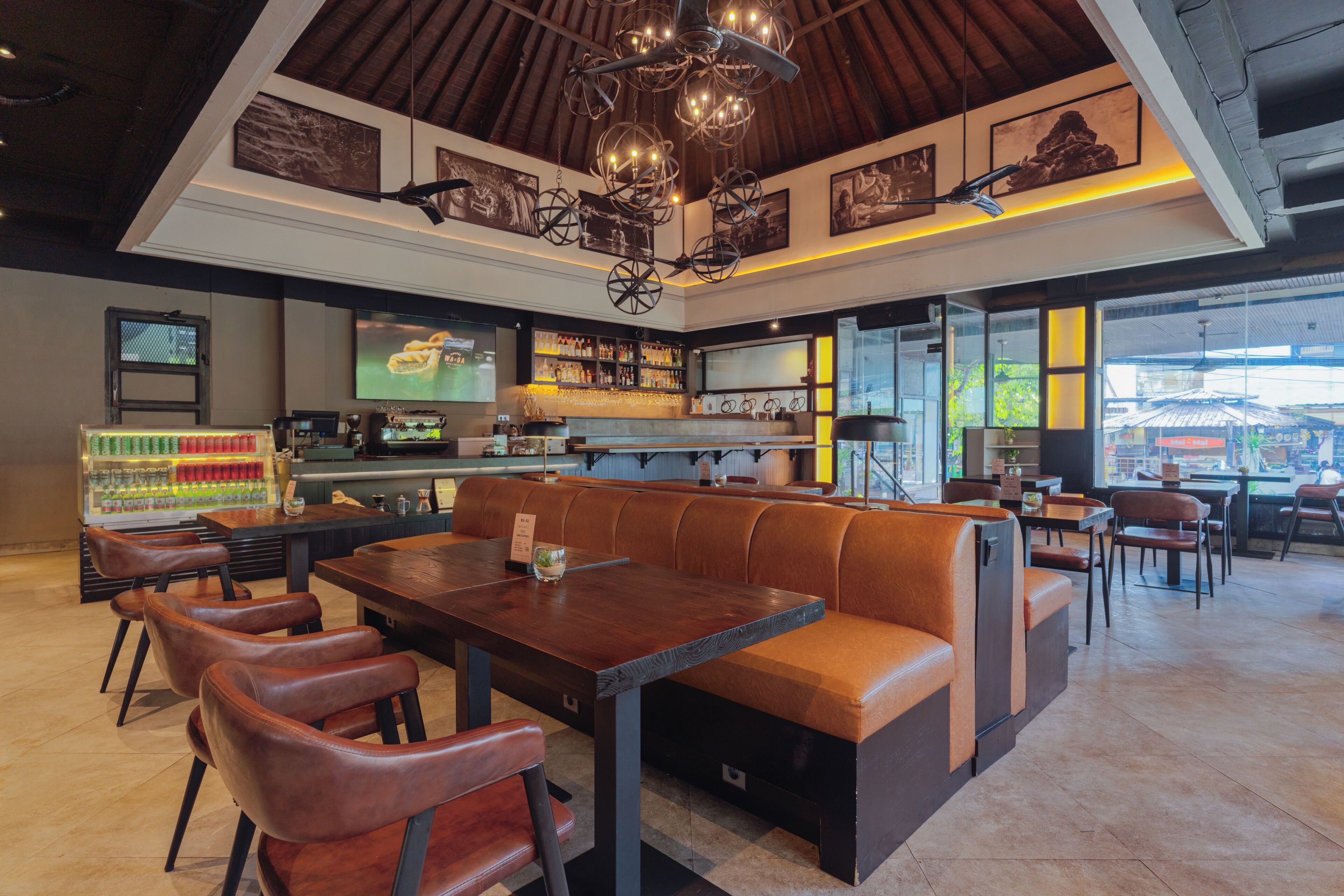 Un restaurante con techos altos, vigas de madera y una zona de bar con estantes llenos de botellas. Hay cabinas de cuero y mesas con sillas.
