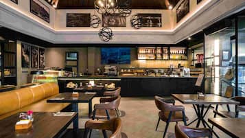 A modern bar area with seating, a counter with a variety of bottles, and artwork on the walls.