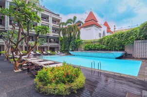 A swimming pool with lounge chairs and a building with a red roof in the background.