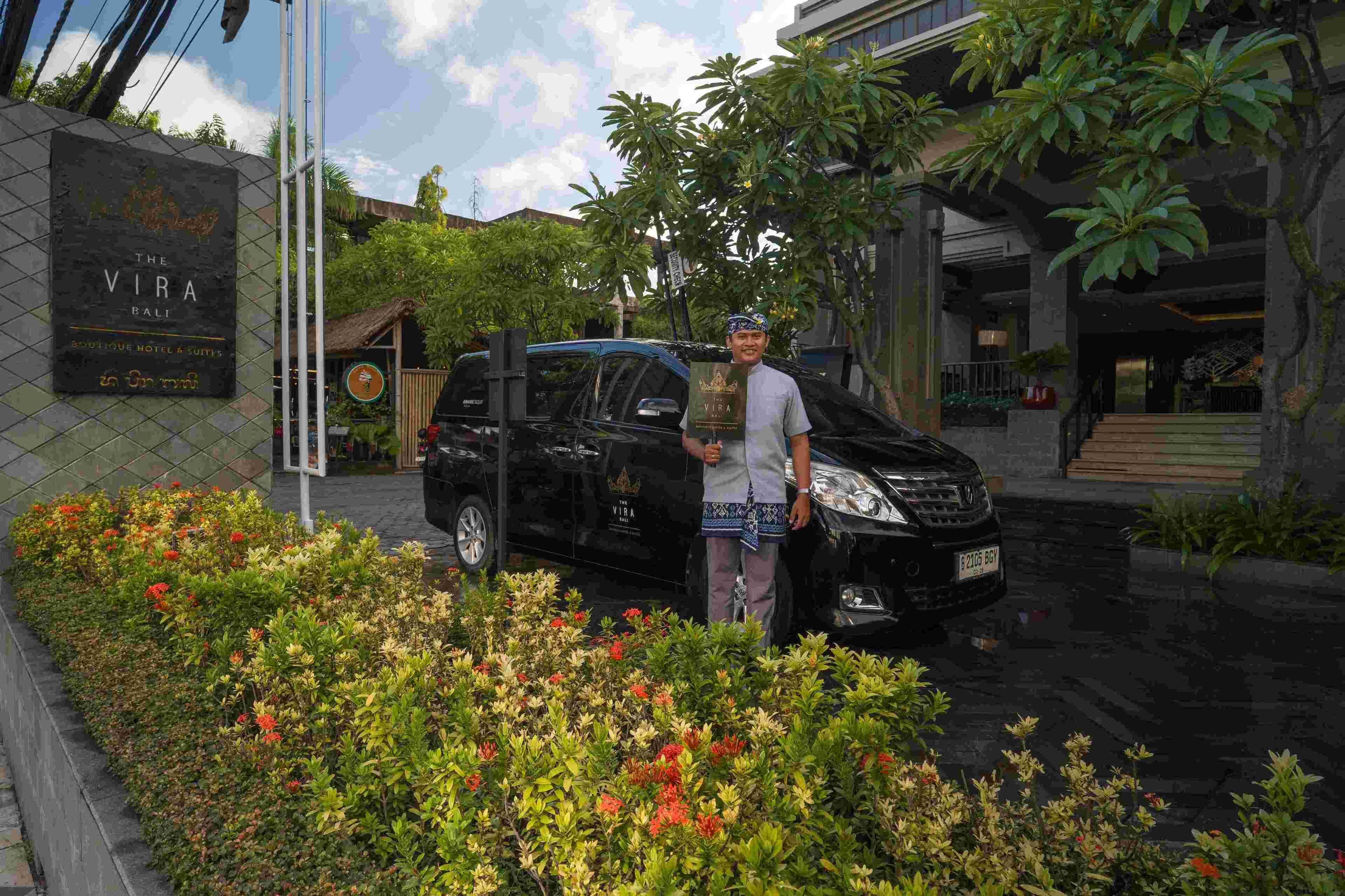 Een man staat naast een zwarte auto voor een hotel genaamd "The Vira Bali".