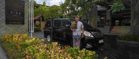 A man standing next to a black car in front of a hotel named "The Vira Bali."