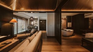 A modern interior with a wooden ceiling, a seating area with a sofa and ottoman, a dining area with a table and chairs, and a bathroom with a bathtub. - The Vira Bali Boutique Hotel & Suite (Kuta)
