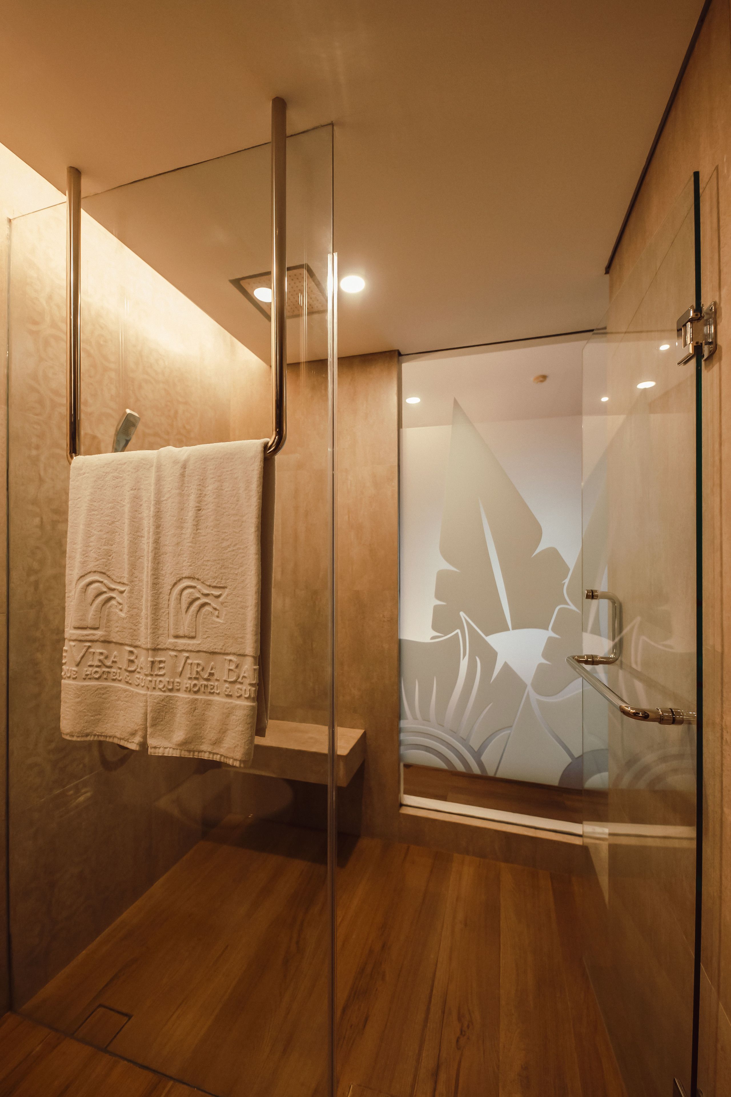 A modern shower with glass doors, a wooden floor, and a towel hanging on a metal rack.