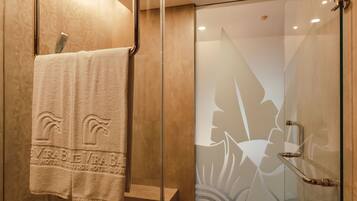 A modern shower with glass doors, a wooden floor, and a towel hanging on a metal rack.