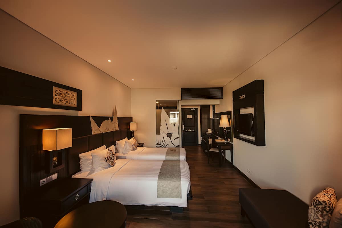 Habitación de hotel con dos camas, un escritorio, una silla y un televisor.