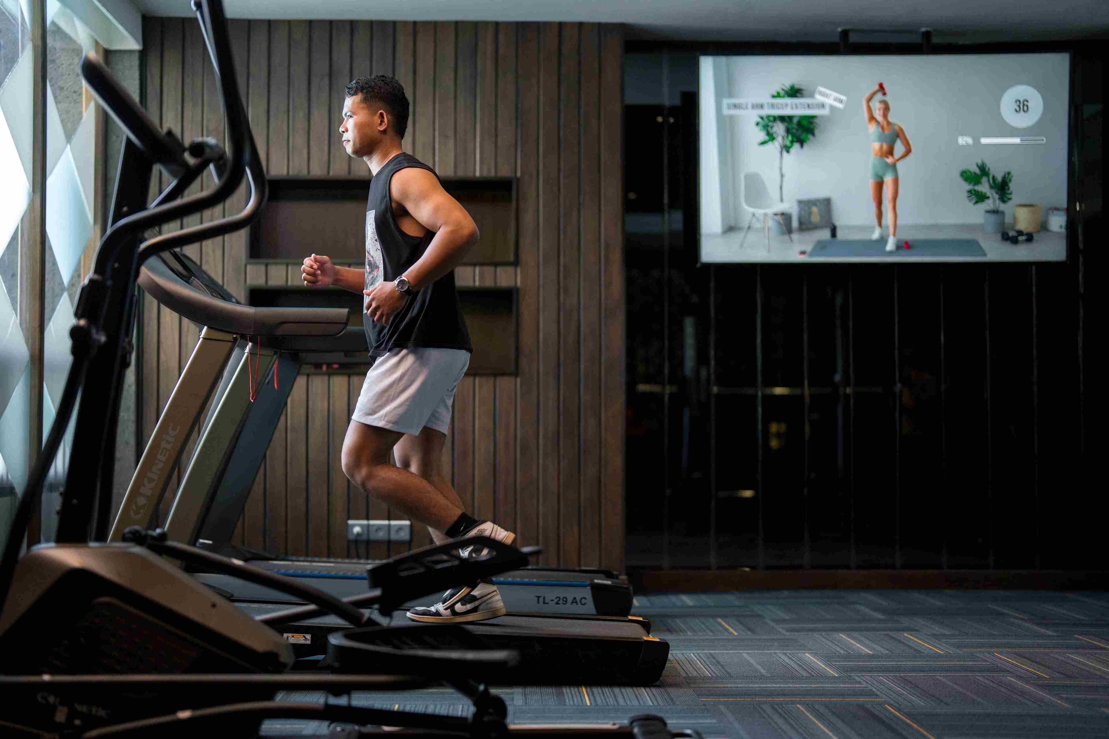 A treadmill in a gym with a projection screen displaying a fitness class.