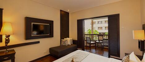 A hotel room with a bed, a TV mounted on the wall, a balcony with a table and chairs, and a lamp on a bedside table.