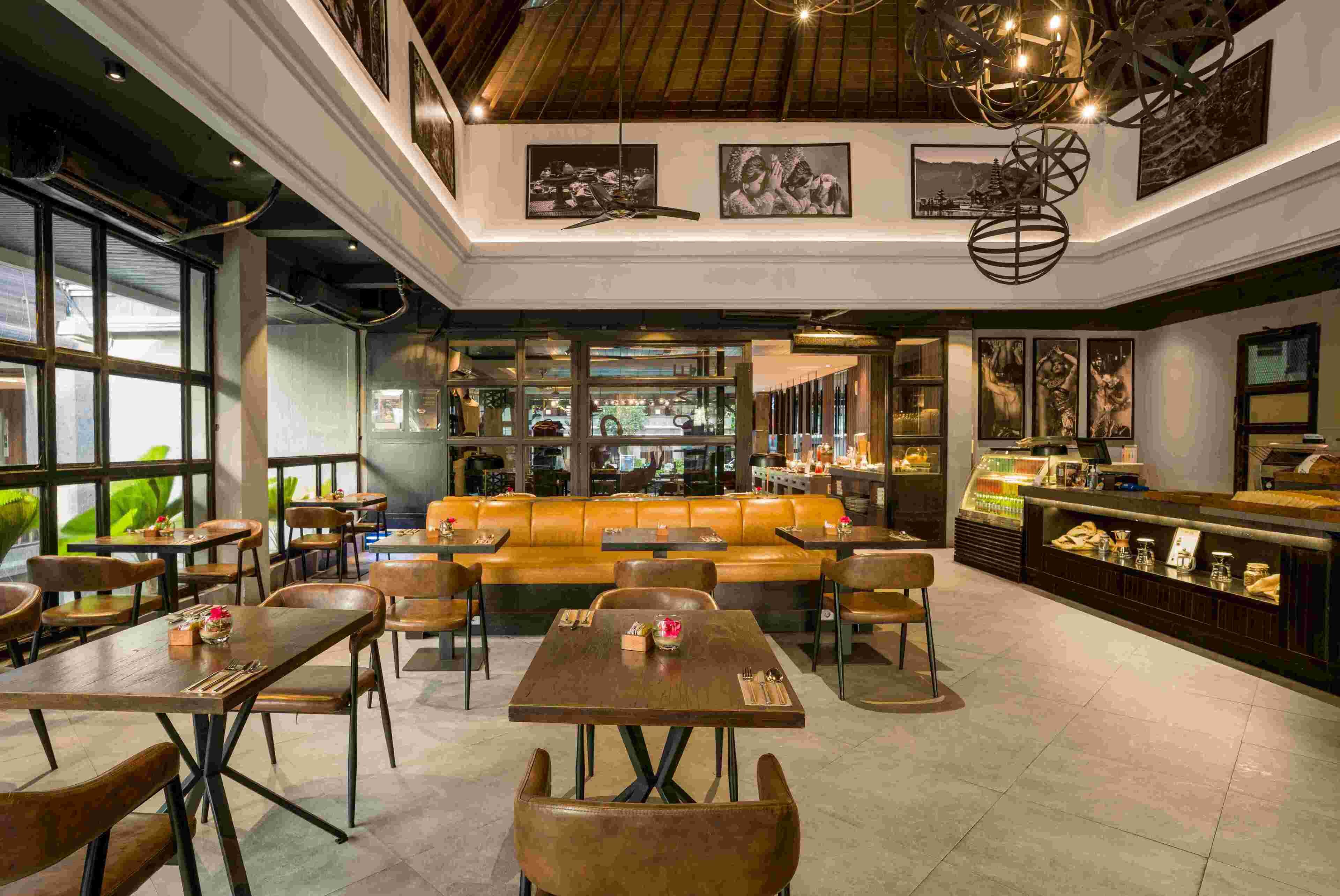 A modern restaurant with a central seating area, a bar, and large windows.