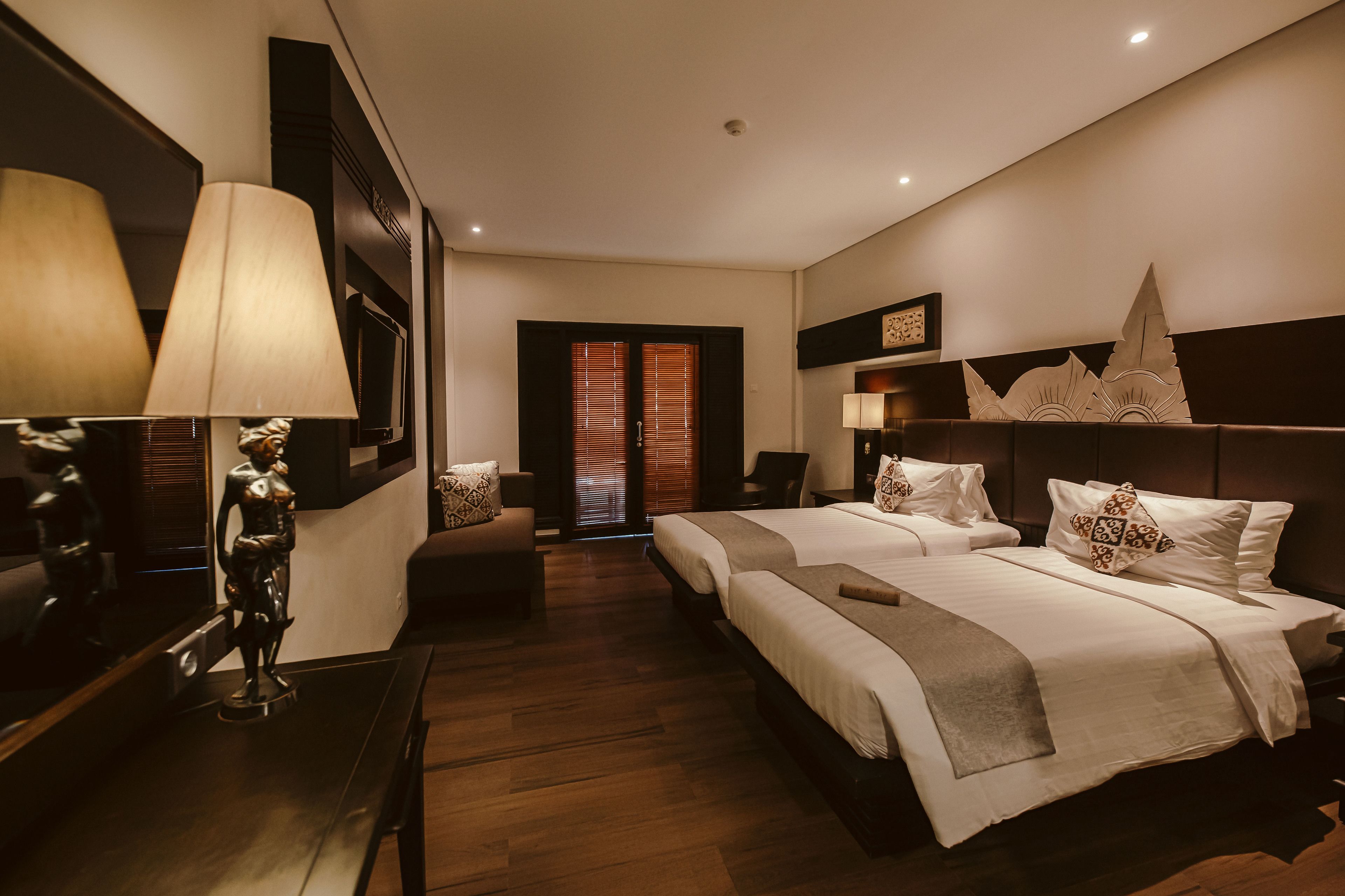 A hotel room with two beds, a desk, a chair, a lamp, and a decorative wall piece.