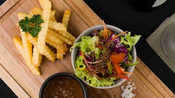 Uma tábua de corte de madeira com uma refeição composta por batatas fritas, salada, bife e molho.